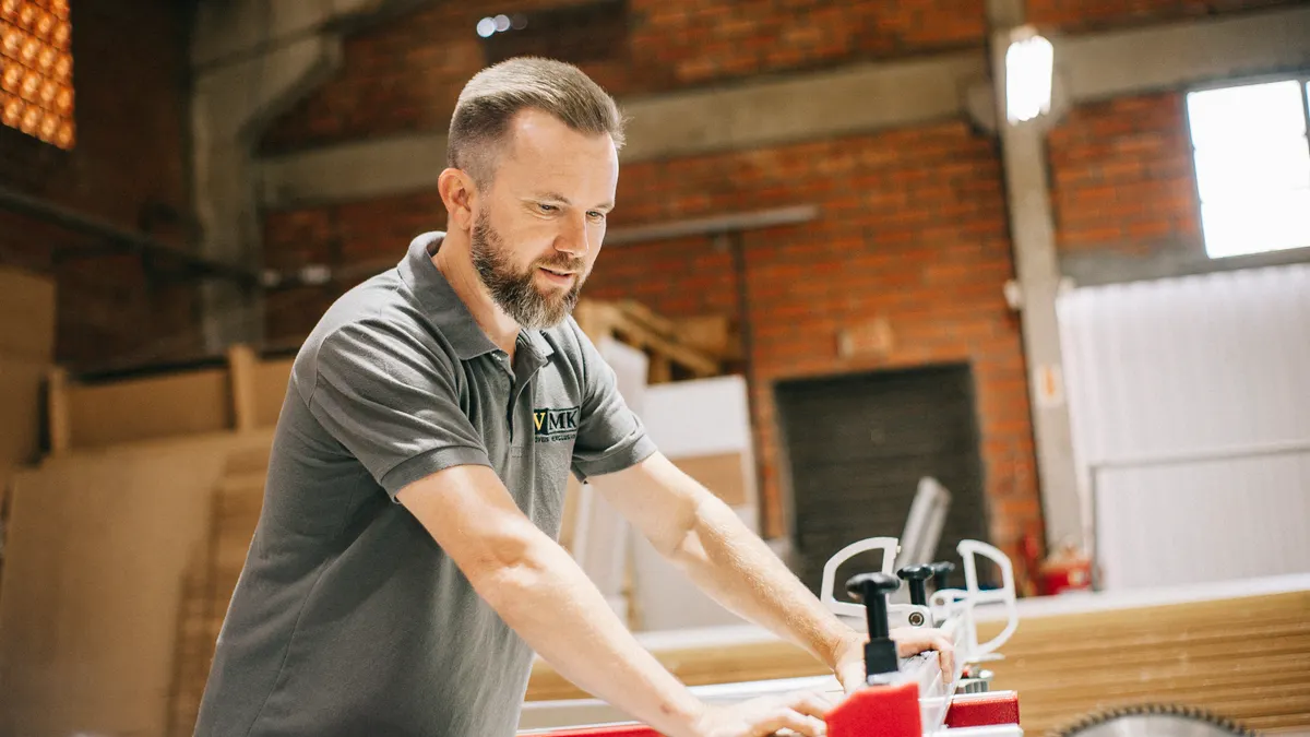 Carpenter guiding a board on a table saw in a woodworking shop