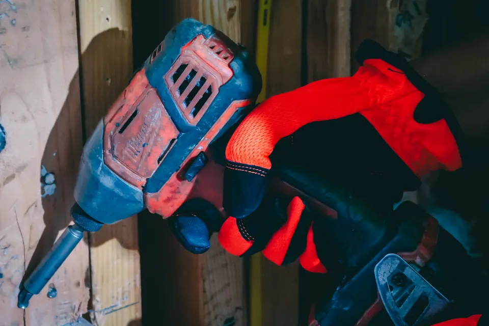 Gloved hand driving screws with a cordless drill into wall framing