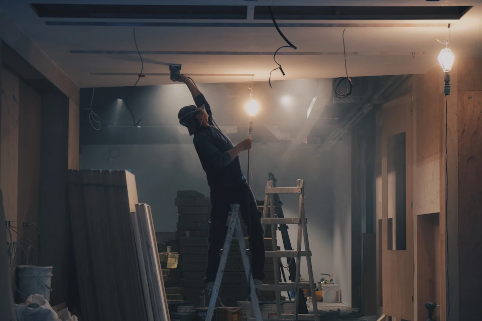 Worker on a ladder finishing ceiling drywall during renovation