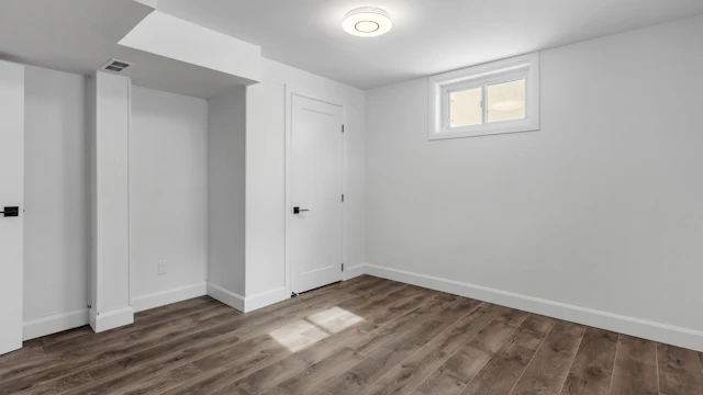 Finished basement room with dark wood-look flooring and white walls